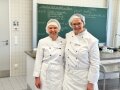 2 Personen in weißer Kleidung stehen in einem Klassenzimmer