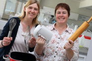 Zwei Lehrkräfte halten verschiedene Küchenutensilien in der Hand